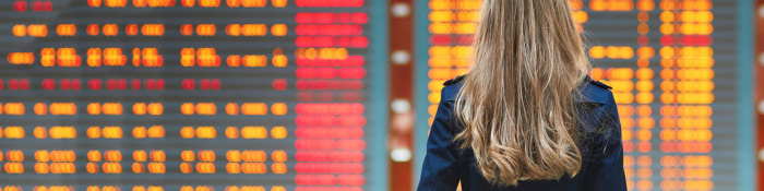 Internationaler Business-Knigge Frau mit Mantel betrachtet Tafel am Flughafen