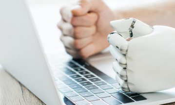 Digital Ethics eine menschliche und eine Roboterhand liegen nebeneinander auf einer Laptop-Tastatur
