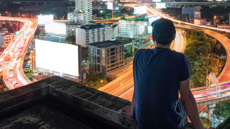Future Readiness Mann sitzt auf Gebäude und blickt auf Skyline in der Nacht