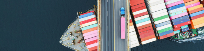 Lieferketten: Frachter mit Ladung fährt unter einer Brücke durch, auf der ein Lastwagen unterwegs ist