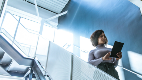 Digitale Transformation: Frau läuft in einem Bürogebäude mit einem Tablet in der Hand eine Treppe herunter.