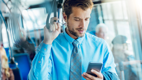ESG: Ein Mann in einem himmelblauen Hemd und blauer Krawatte steht in einem Bus und schaut auf sein Smartphone.