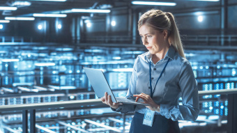 Cloud Computing: Frau steht in einer Halle mit Neonlicht und scrollt auf ihrem Laptop