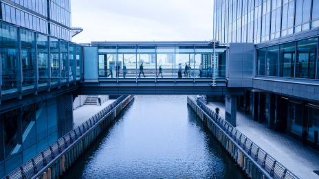 Governance & Compliance: Zwischen zwei Bürogebäuden führt ein Gang über einen Fluss.