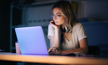 Eine Frau sitzt in einem Büro konzentriert vor einem aufgeklappten Laptop. 