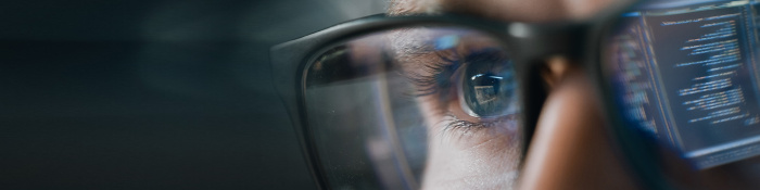 Gesicht mit Brille, bei einem Brillenglas spiegeln sich Daten von einem Bildschirm 