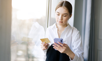 Junge Frau schaut auf ihr Handy und hält Kreditkarte in der Hand