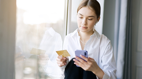 Junge Frau schaut auf ihr Handy und hält Kreditkarte in der Hand