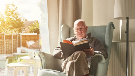 älterer Mann sitzt im Sessel und liest ein Buch 