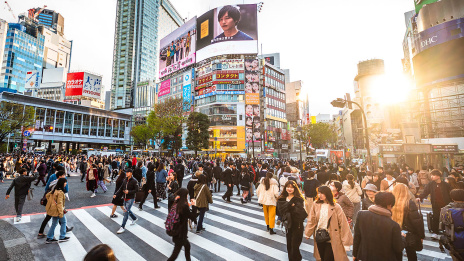 Viele Menschen gehen über eine Kreuzung in einer japanischen Großstadt.