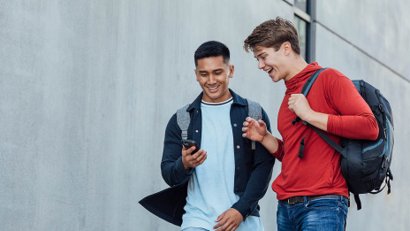 Zwei junge Männer schauen gemeinsam auf ein Handy, das einer von ihnen in der Hand hält.