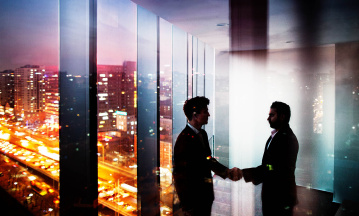 Zwei Männer diskutieren in einem Hochhaus bei Nacht. 