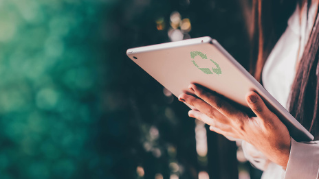 Eine Hand hält ein Tablet auf dem ein grünes Nachhaltigkeitssymbol zu sehen ist. 