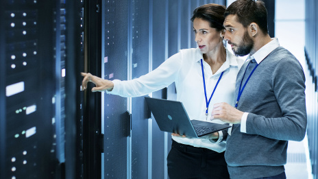 Digitale Transformation: Ein IT-Spezialist steht mit einer Technikerin in einem Rechenzentrum vor einem offenen Rack-Server-Schrank, er hält einen Laptop.