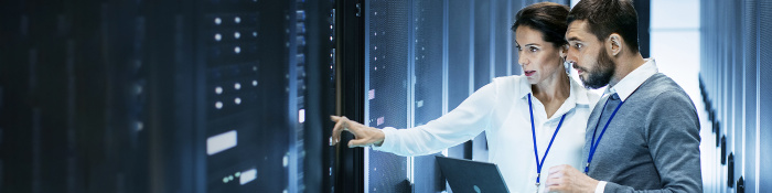 Digitale Transformation: Ein IT-Spezialist steht mit einer Technikerin in einem Rechenzentrum vor einem offenen Rack-Server-Schrank, er hält einen Laptop.