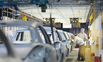 Automobilindustrie: Beschäftigte arbeiten in einer Industriehalle an einem Auto.