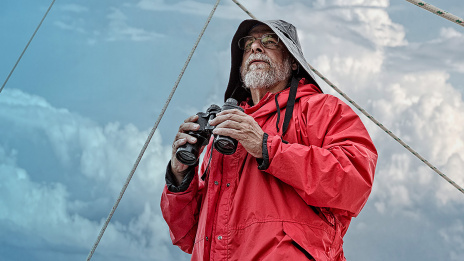 Ein Mann am Bug eines Segelbootes überblickt die Überprüfung der Meere und des Wetters.