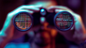 Cybersicherheit: Hacker hält Fernglas in der Hand und nimmt Daten von Unternehmen ins Visier.