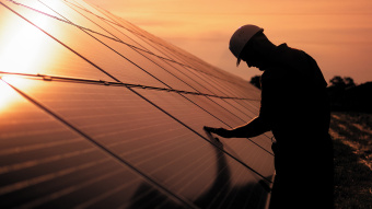 Energiewende: Ein Assistenztechniker in Uniform berührt Sonnenkollektoren bei Sonnenuntergang mit der Hand.