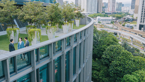 ESG: Geschäftsleute diskutieren in einem grünen Garten auf einem Hochhausdach.