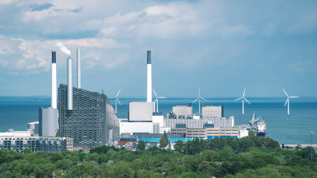 Klimaneutrale Fabrik: Eine Produktionsstätte mit rauchendem Schornstein, davor ein Wald.