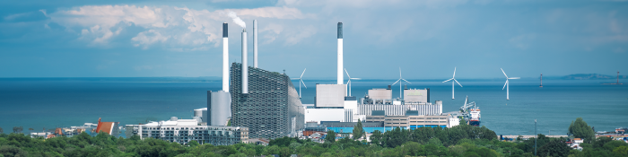 Klimaneutrale Fabrik: Eine Produktionsstätte mit rauchendem Schornstein, davor ein Wald.