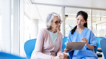 Krankenschwester guckt mit älterer Frau auf Tablet im Wartezimmer