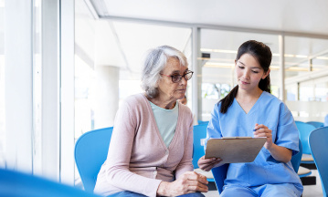 Krankenschwester guckt mit älterer Frau auf Tablet im Wartezimmer