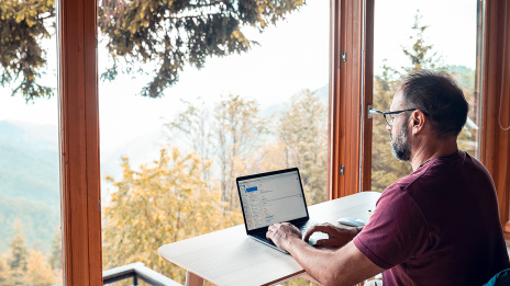 Remote Work: Ein Mann sitzt am Laptop und schaut aus dem Fenster. Er arbeitet am Urlaubsort.