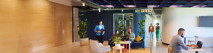 Unternehmenskultur: Das Foto zeigt Menschen an ihrem Arbeitsplatz, der offen gestaltet ist mit Sitzgruppen, Einzeltischen, Pflanzen. 