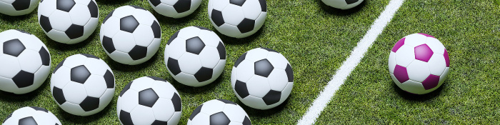 Ein lilafarbener Fußball liegt neben einer Linie, hinter liegen in Reih und Glied schwarz-weiße Fußbälle