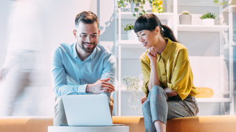 Partnerschaftliche Zusammenarbeit: Ein Mann (links) und eine Frau (rechts) blicken gemeinsam auf einen Laptop.