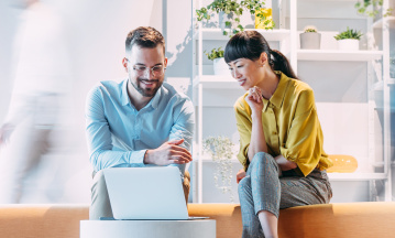 Partnerschaftliche Zusammenarbeit: Ein Mann (links) und eine Frau (rechts) blicken gemeinsam auf einen Laptop.