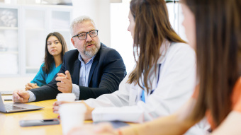 Krankenhausreform: Ärzte und Pfleger sitzen an einem Schreibtisch in einer Klinik und diskutieren Themen rund um das Gesundheitswesen.