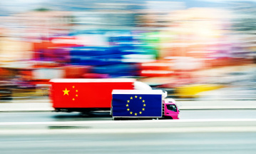 Zwei LKW nebeneinander. Einer mit einer europäischen Flagge, einer mit einer chinesischen. Der mit der europäischen Flagge liegt leicht in Führung. 