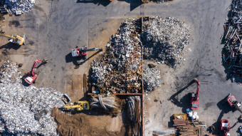 Drohnenaufnahme einer Recyclinganlage mit mehreren Baggern und sortiertem Metallschrott.
