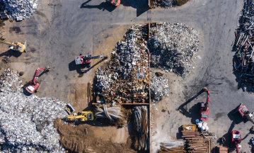 Drohnenaufnahme einer Recyclinganlage mit mehreren Baggern und sortiertem Metallschrott.