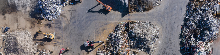 Drohnenaufnahme einer Recyclinganlage mit mehreren Baggern und sortiertem Metallschrott.