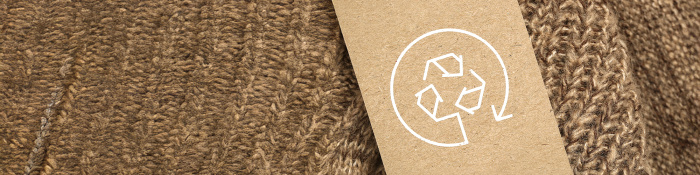 Nahaufnahme eines braunen Strickkleidungsstücks mit einem Kartonetikett, das ein weißes Recycling-Symbol zeigt.