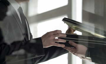 Zwei Männer in Anzügen übergeben sich in einem Büro diskret einen offenen Aktenkoffer – symbolisches Bild für geheime Geschäfte, Korruption oder Wirtschaftskriminalität.