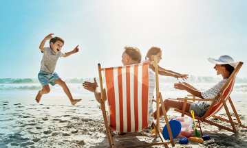 Strandbild mit rot-weiß gestreiftem Sonnenstuhl, Familie mit zwei Kindern, kleiner Junge springt, Eltern sitzen auf Strandstühlen