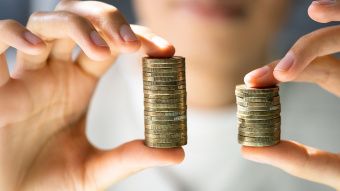 Symbolbild zur Entgelttransparenzrichtlinie: Person hält zwei ungleiche Stapel mit Münzen in den Händen