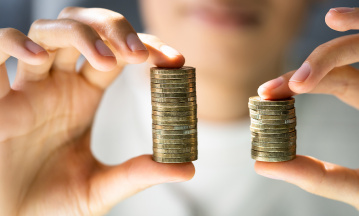 Symbolbild zur Entgelttransparenzrichtlinie: Person hält zwei ungleiche Stapel mit Münzen in den Händen