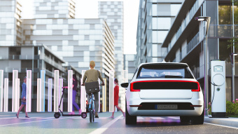Ein Elektroauto steht in einer futuristischen Stadtlandschaft an einer Ladesäule. Daneben eine Radfahrerin. 