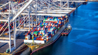 Handelsabkommen zwischen der EU und den USA: Container stapeln sich auf einem Frachtschiff, das im Hafen liegt. Zu sehen sind diverse Kräne.