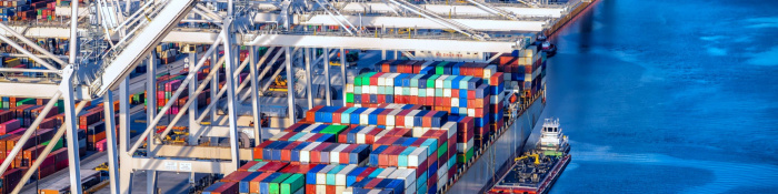 Handelsabkommen zwischen der EU und den USA: Container stapeln sich auf einem Frachtschiff, das im Hafen liegt. Zu sehen sind diverse Kräne.