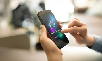 Vier Menschen sitzen um einen Konferenztisch, eine fünfte männliche Person steht hinter dem Konferenztisch neben einem Screen, auf dem mit weißer Schrift "Artificial Intelligence" steht. 