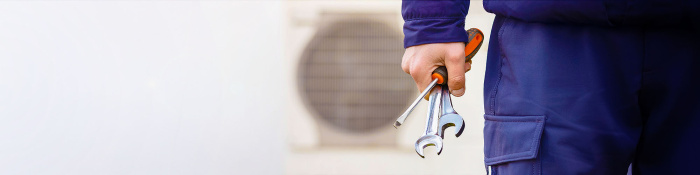 Servicetechniker in Arbeitskleidung hält Werkzeug in der Hand und steht vor einer Wärmepumpe.