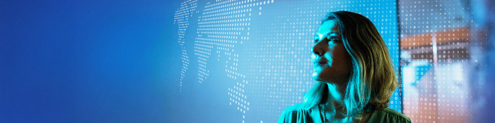 Frau im Profil blickt nach rechts vor einem blauen, digitalen Hintergrund mit abstrahierter Weltkarte aus Punkten. Die Szene vermittelt Zukunftsorientierung, Datenanalyse und technologische Transformation im Audit-Umfeld.