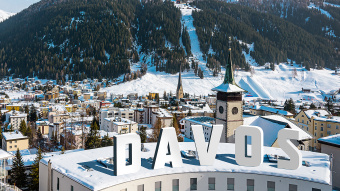 Ein Bergpanorama mit Häusern, Schnee und Wäldern, auf einem Schrfitzug steht Davos.